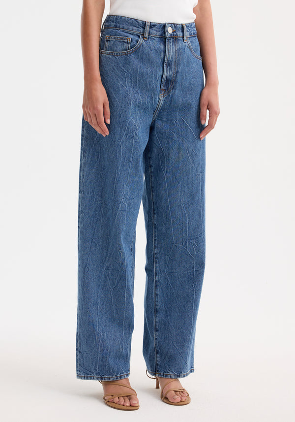 Signature baggy fit denim | mid denim blue jeans, featuring a high-waisted wide-leg style, paired with tan strappy sandals against a plain white background.