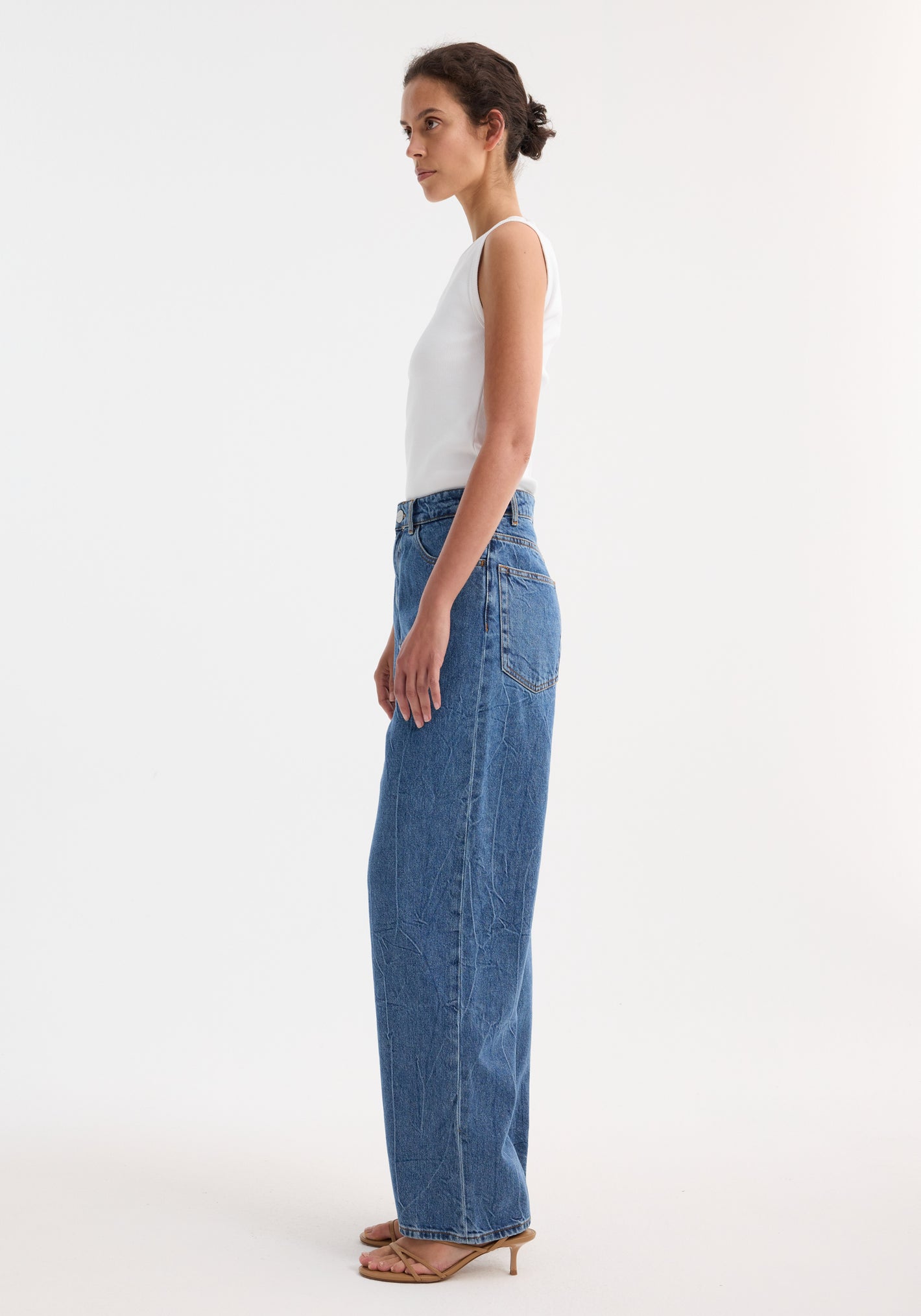 Young woman wearing Signature baggy fit denim in mid denim blue, featuring low-waist, wide-leg style, paired with a fitted sleeveless top and tan sandals.