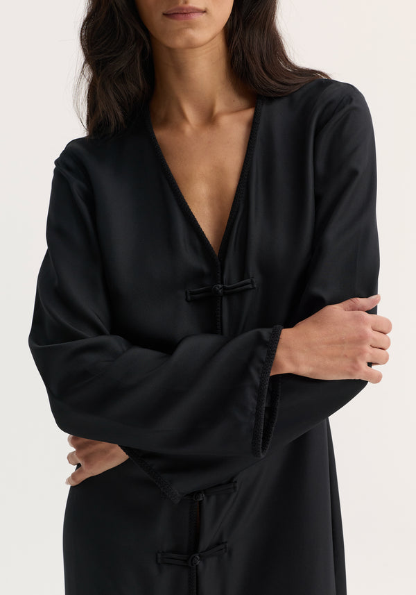 Mandarin silk dress | black: Woman in a black, long-sleeved robe-style dress with a V-neck and pankou closures, arms crossed, studio shot.