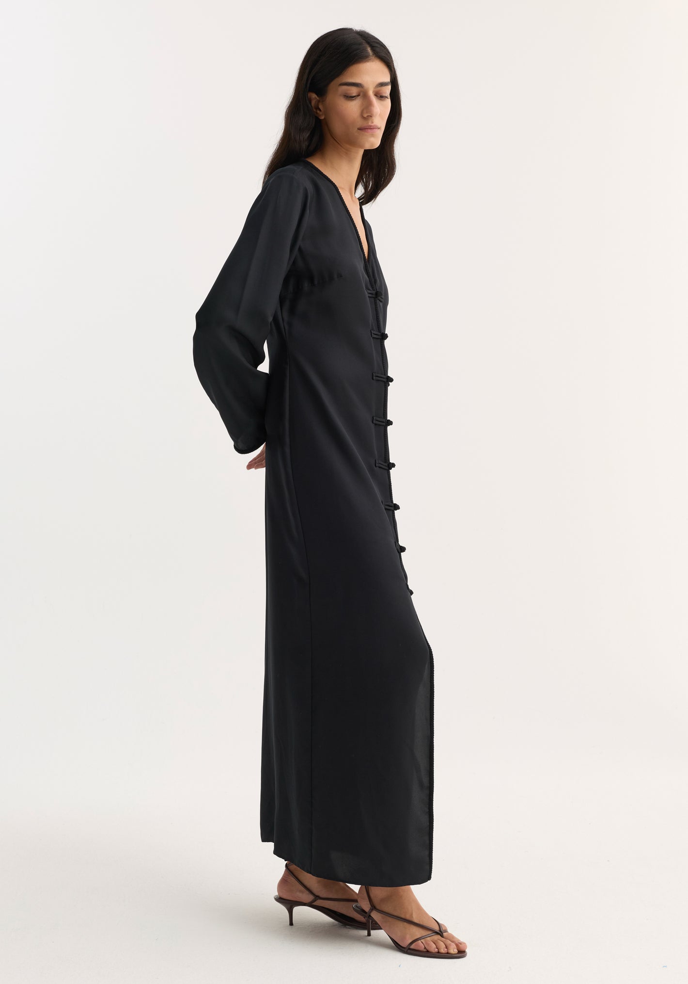 Mandarin silk dress | black: A slim woman in a black, V-neck, pure silk maxi dress with pankou closures, long sleeves, and a high front split.
