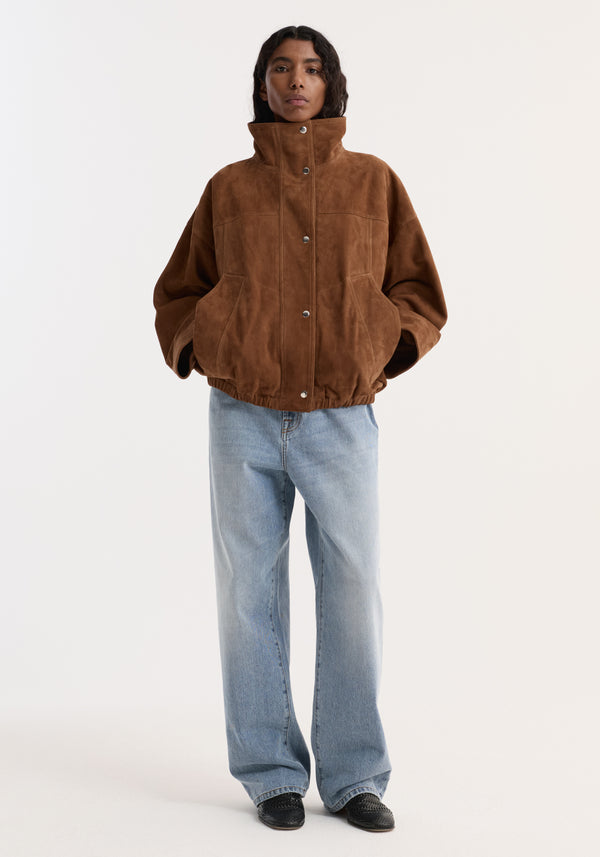Person wearing the Reinvented suede jacket | cognac, featuring a boxy, oversized fit with a statement stand collar and snap-front closure, paired with jeans.