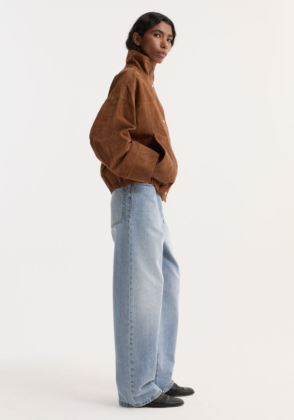 Model wearing Reinvented suede jacket | cognac with high collar and snap-front closure, paired with wide-leg jeans and pointed-toe black shoes.