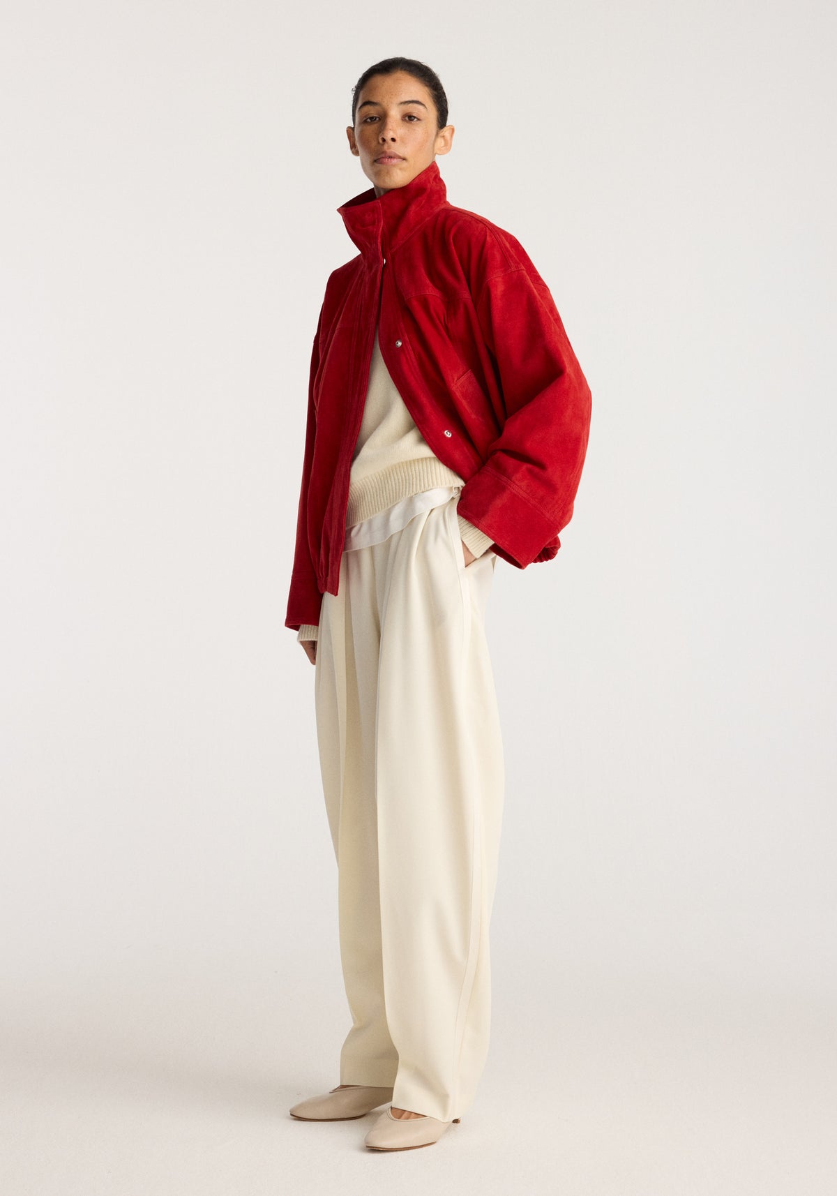 Reinvented suede jacket | red worn by a model with a cream sweater and wide leg trousers in a studio setting