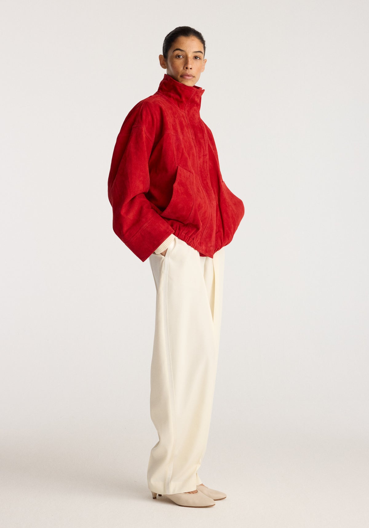 Reinvented suede jacket | red worn with cream trousers and neutral shoes in a studio portrait pose