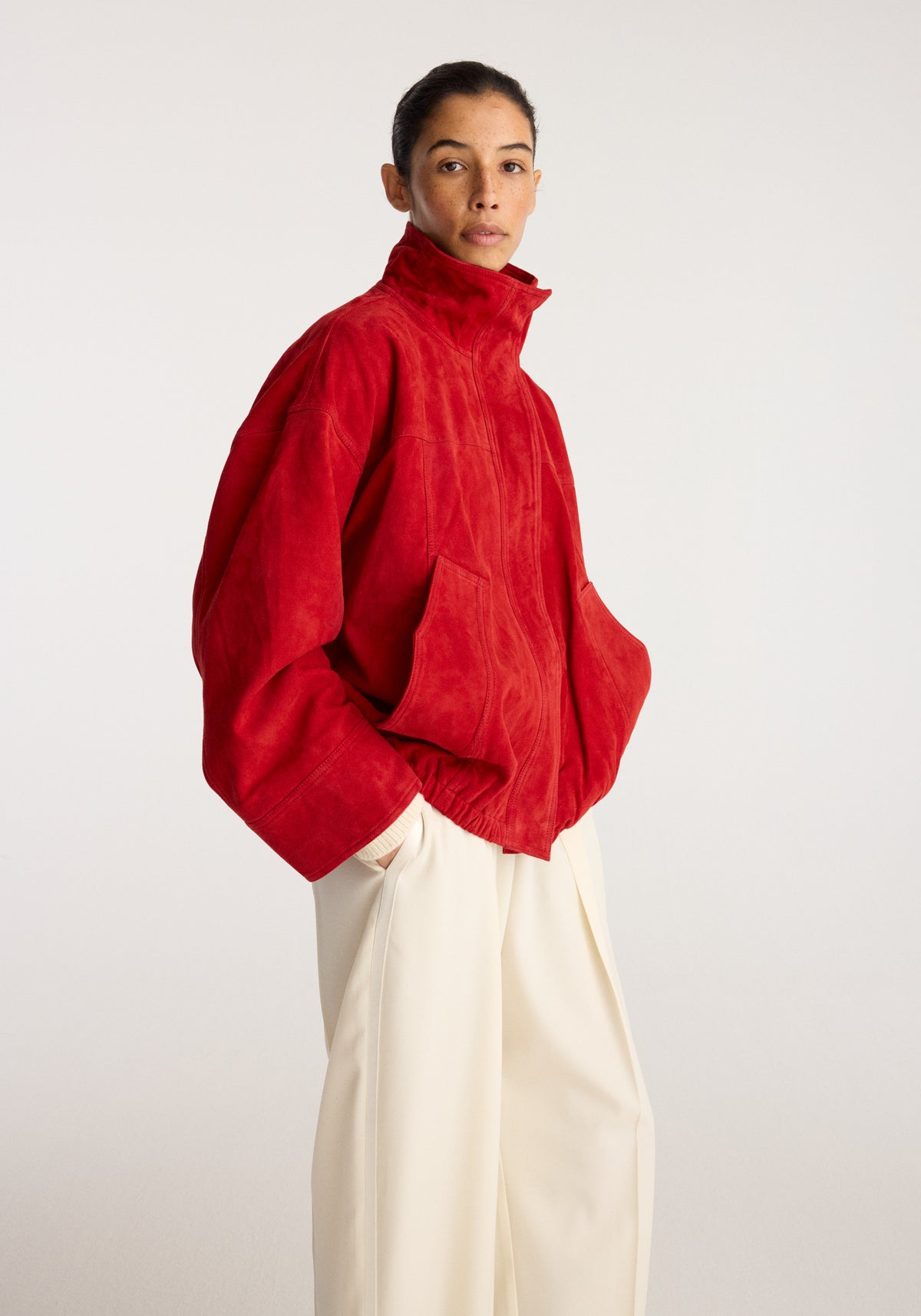 Reinvented suede jacket | red worn by a model with a high collar long sleeves and front pockets styled with cream trousers
