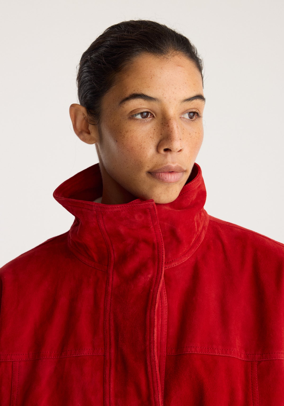 Reinvented suede jacket | red worn by a model with a high stand collar and front zip in a close up portrait