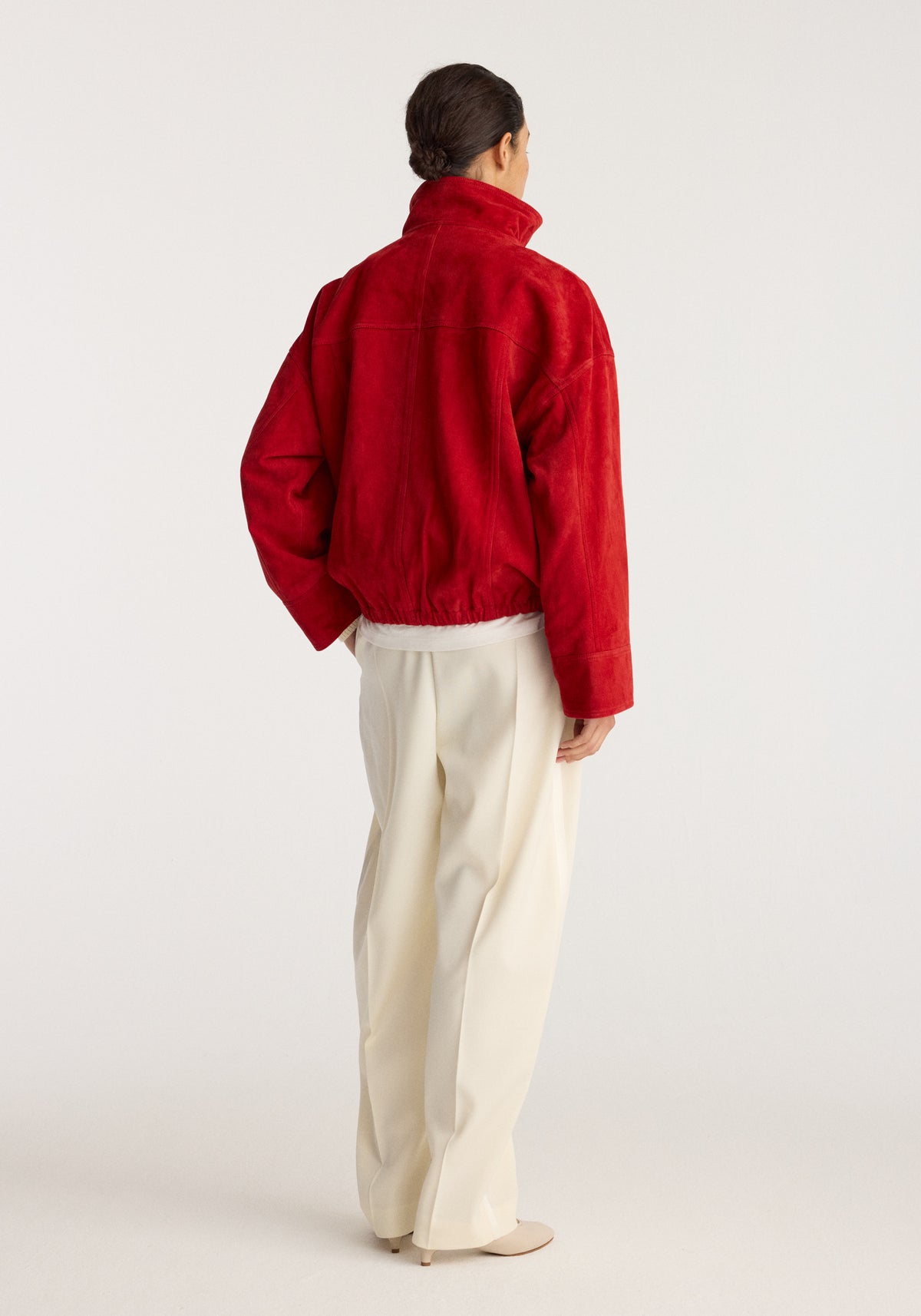 Reinvented suede jacket | red shown from the back on a model wearing cream trousers and neutral shoes in a studio setting