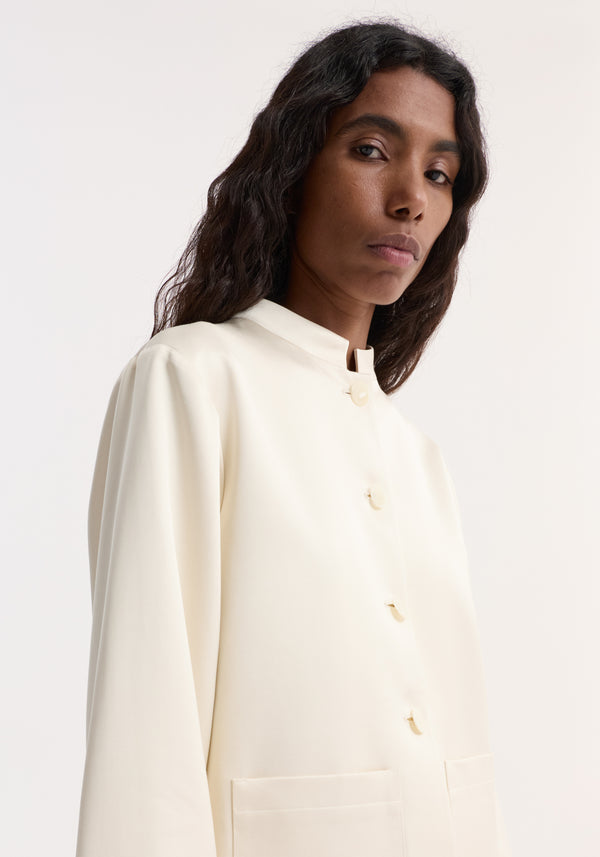 Person wearing Pearl button satin jacket | cream with a stand-up collar, pearl buttons, and front patch pockets, highlighting the satin's smooth texture.