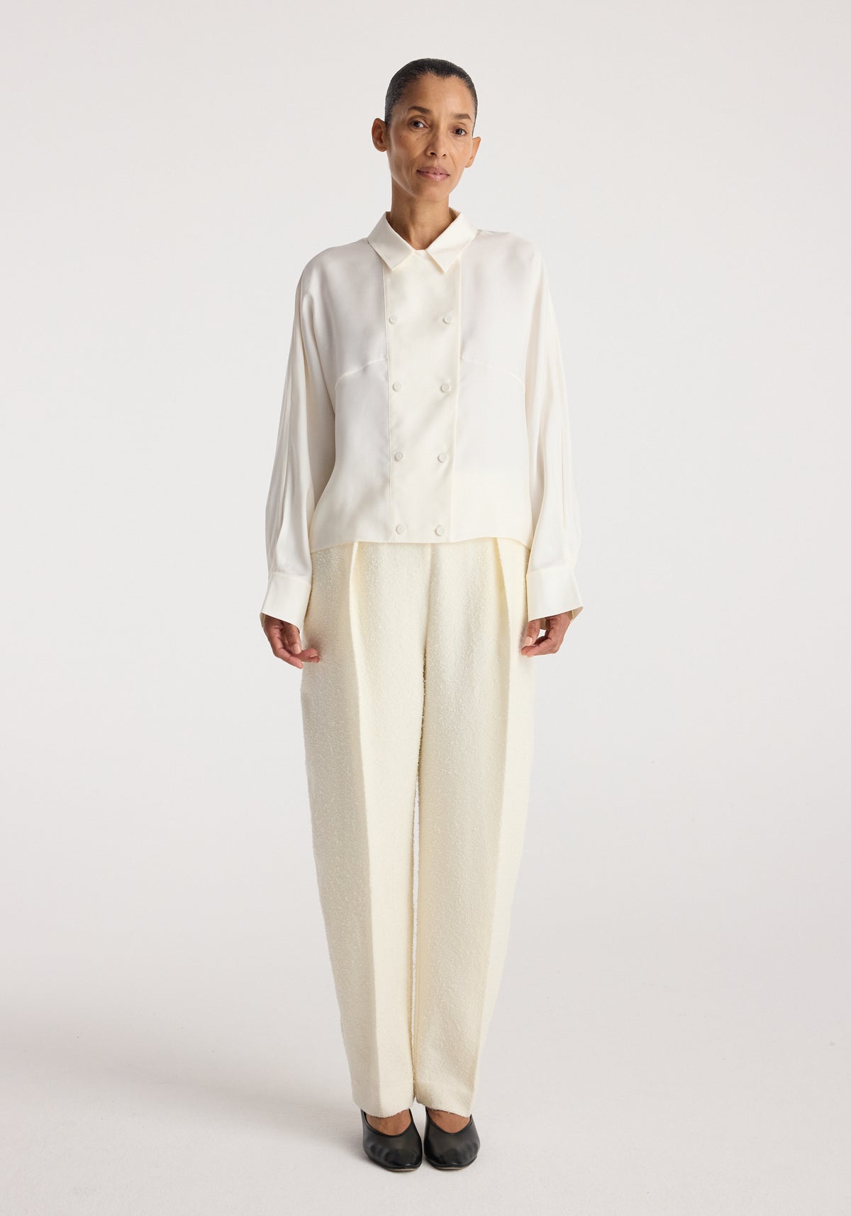 Double breasted silk top | cream worn by a model with long sleeves, pointed collar, button front, and relaxed fit styled with matching cream trousers and black shoes