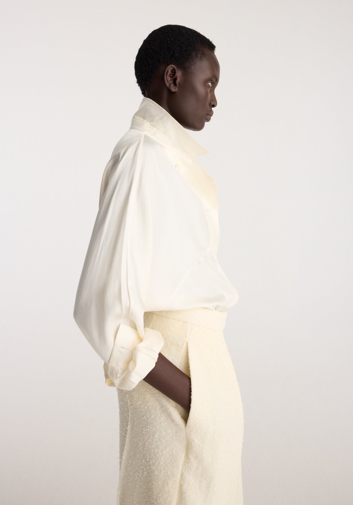 Model in side profile wearing the Double breasted silk top | cream with voluminous sleeves and a high collar styled with cream textured trousers