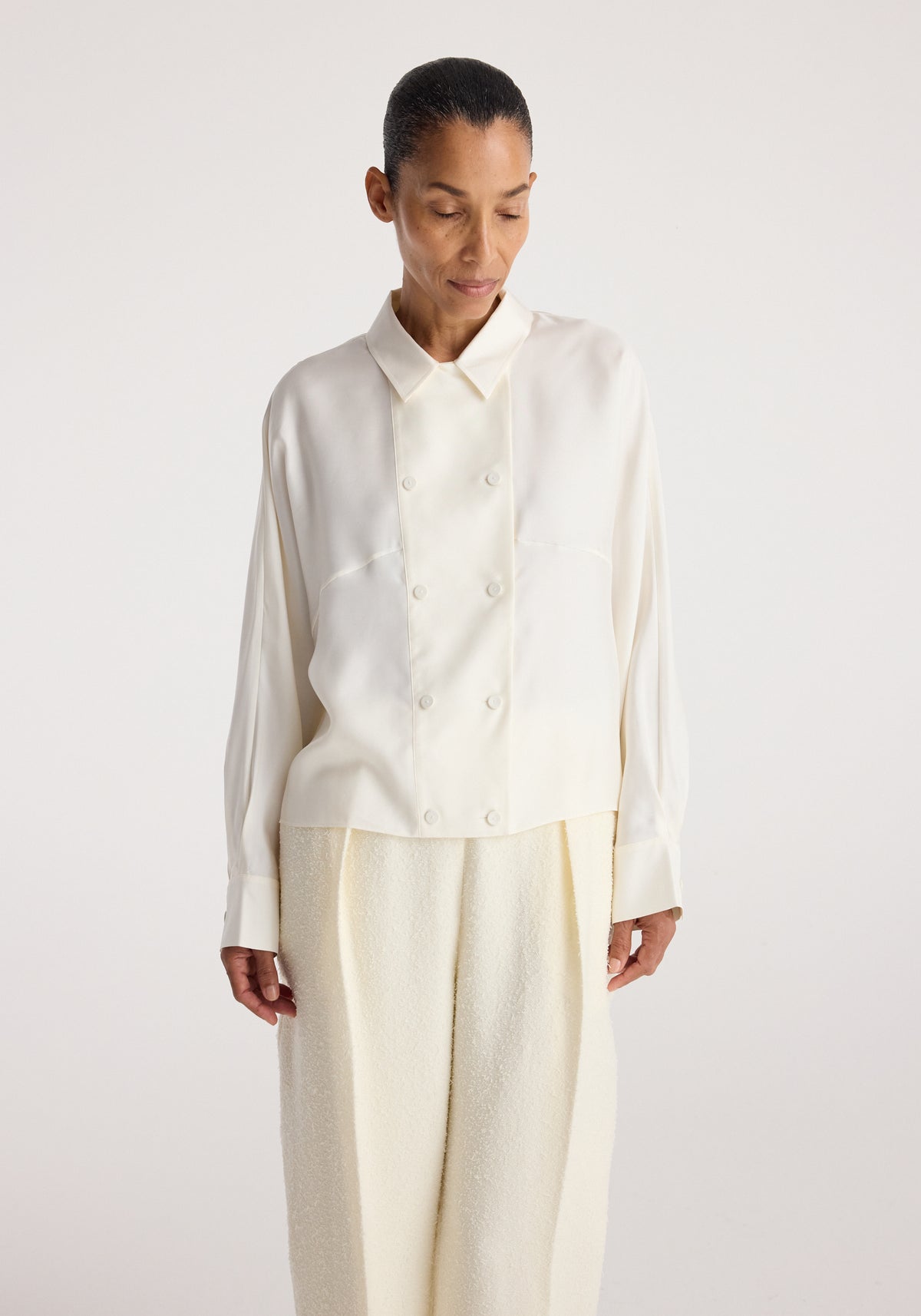 Model wearing Double breasted silk top | cream, a long sleeve cream silk top with pointed collar and double breasted buttons, styled with light trousers