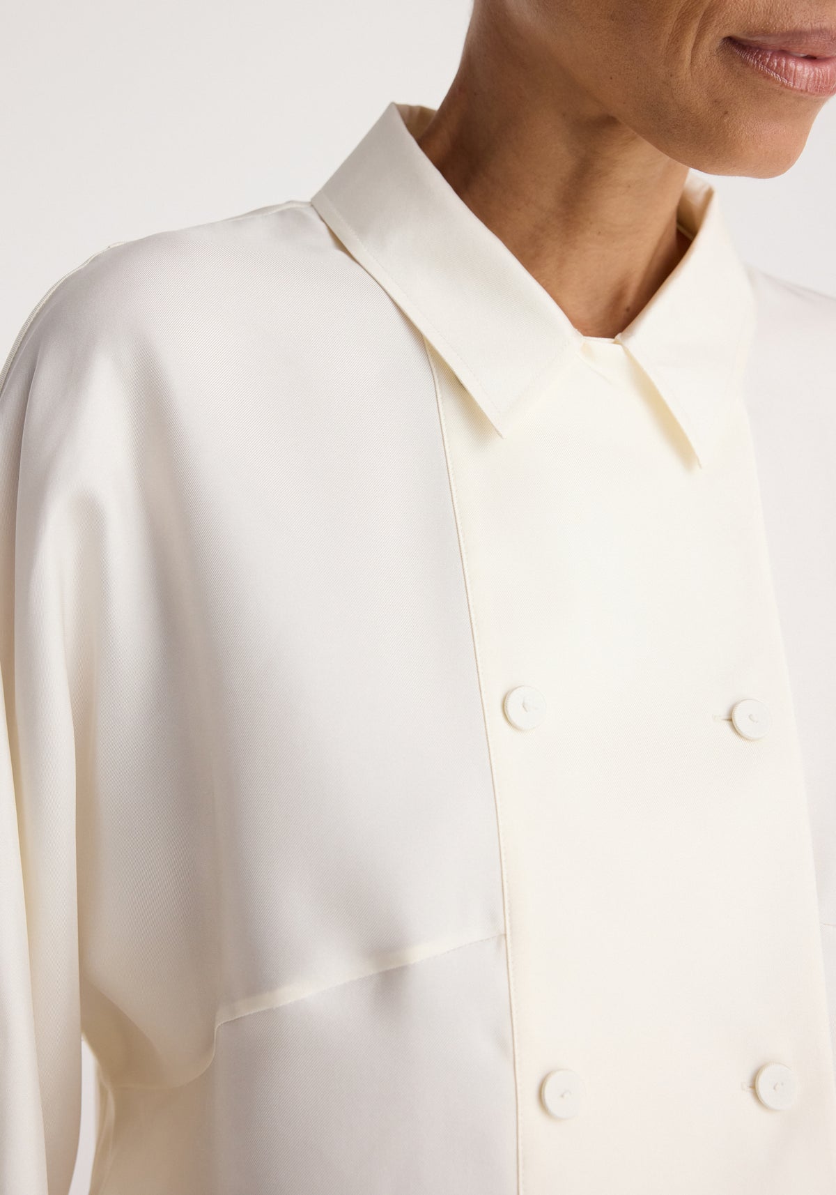 Double breasted silk top | cream shown in close-up on a model, featuring a pointed collar, long sleeves, smooth silk fabric, and covered double-breasted buttons