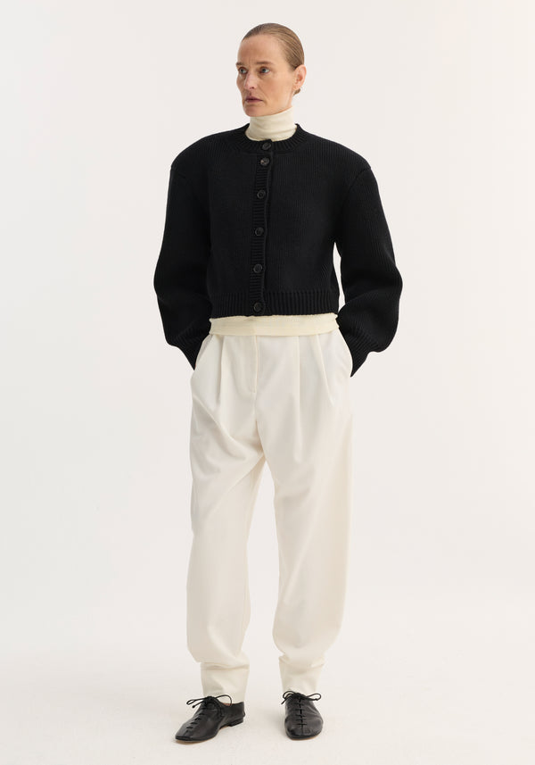 Model wearing Statement shoulder cardigan | black, featuring a cropped, chunky-knit design with large buttons and sharp, structured shoulders, layered over a turtleneck.