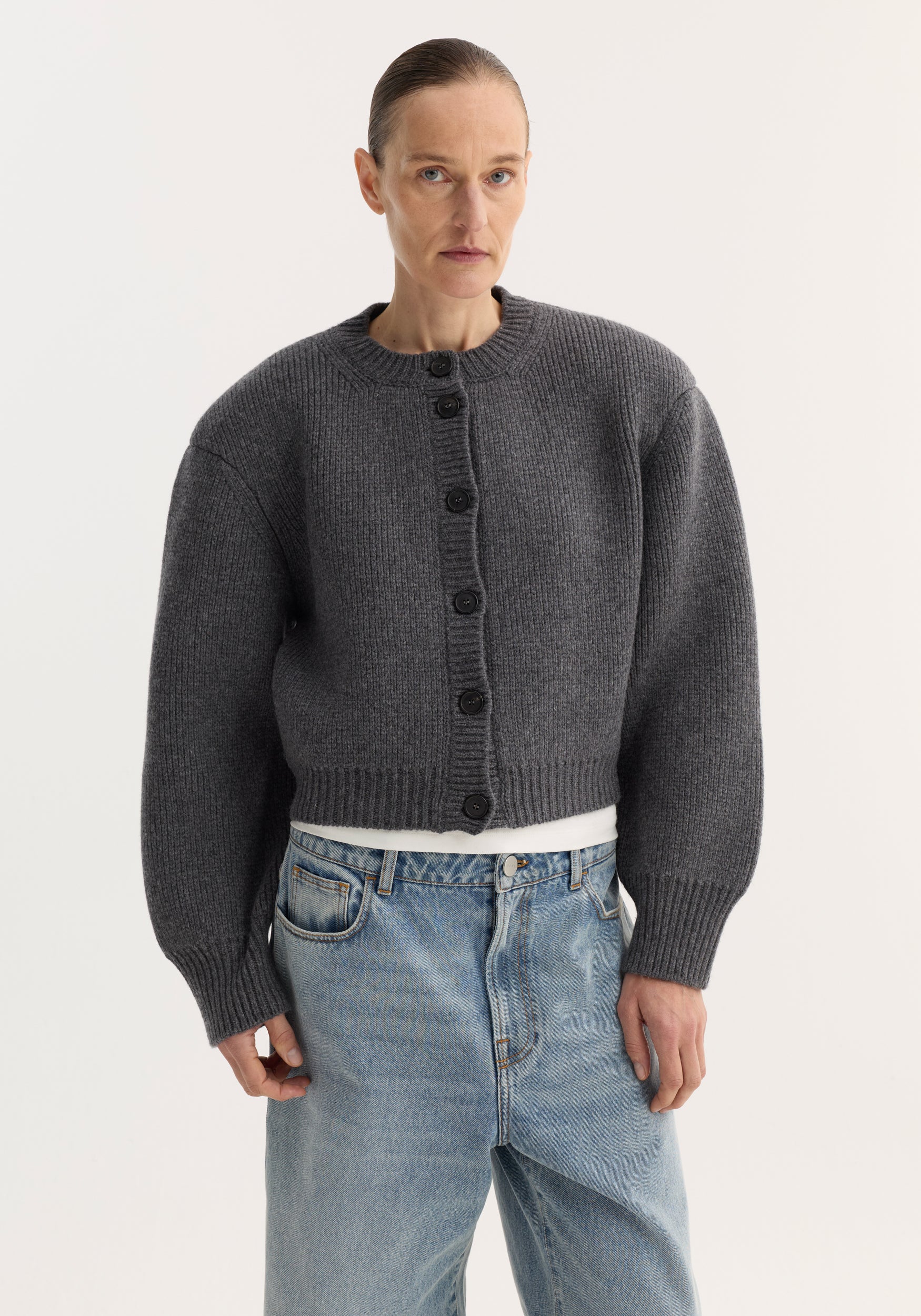 Model wearing a mid grey melange chunky knit button-up with dropped, structured shoulders and ribbed cuffs paired with light blue denim jeans, showcasing the Statement shoulder cardigan | mid grey melange.