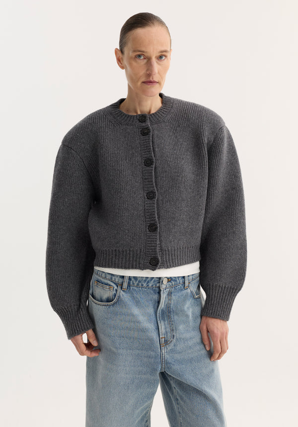 Model wearing Statement shoulder cardigan in mid grey melange, featuring ribbed knit, black button closure, and oversized fit, paired with light-wash, high-rise jeans.