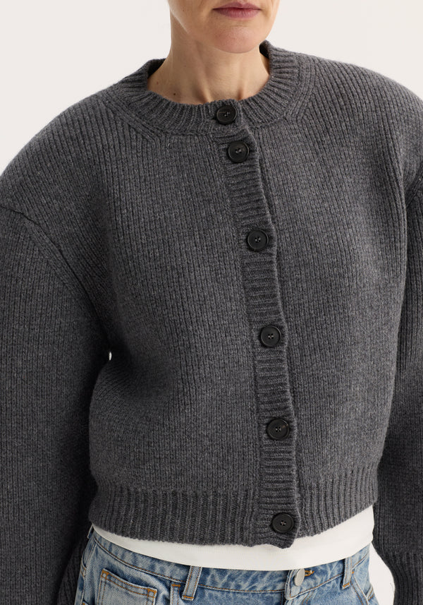 Statement shoulder cardigan in mid grey melange with ribbed knit, oversized fit, structured shoulders, and button row closure, layered over a white top and jeans.