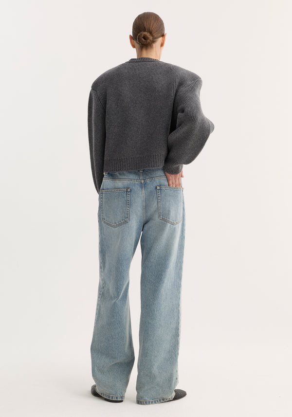 Person in a chunky knit Statement shoulder cardigan with dropped shoulders and wide-leg jeans, showcasing the cardigan's oversized fit and sculptural design.