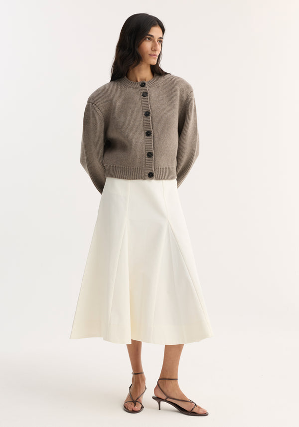 Model wearing Statement shoulder cardigan in clay melange with ribbed details, paired with a high-waisted A-line midi skirt and strappy kitten heel sandals.