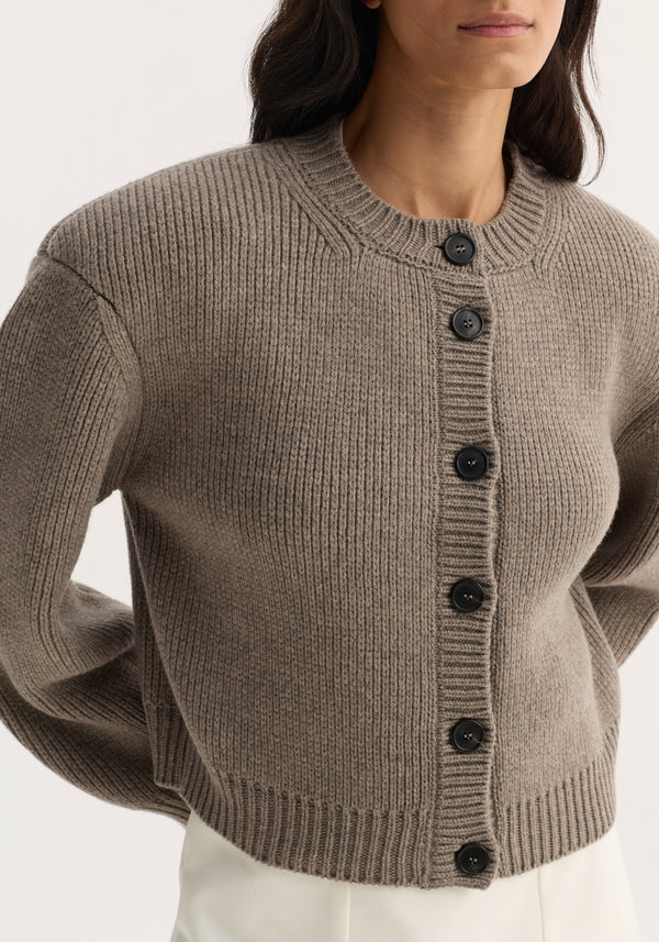 Model wearing the Statement shoulder cardigan in clay melange, featuring a chunky rib-knit design with matte-black buttons and an oversized fit, emphasizing structured shoulders.