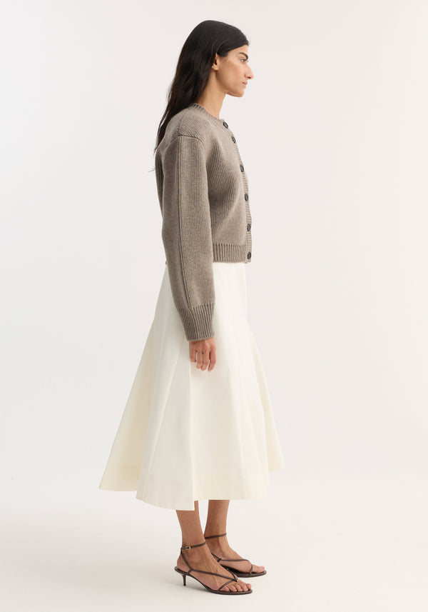Woman in profile wearing a Statement shoulder cardigan in clay melange, featuring an oversized fit and button closure, paired with a midi skirt and strappy sandals.