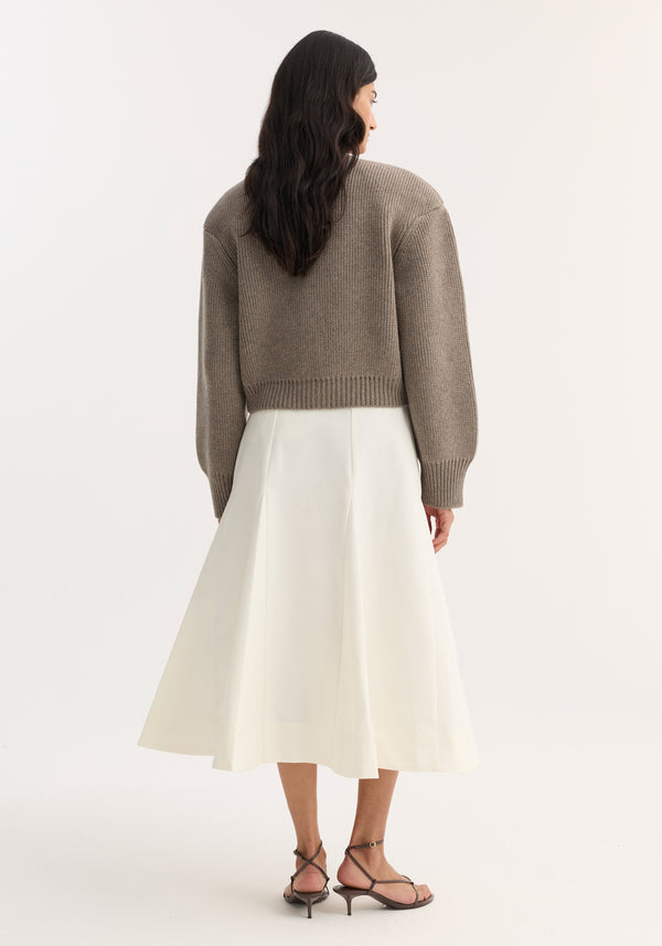 Woman wearing Statement shoulder cardigan in clay melange, with dropped shoulders and oversized fit, paired with high-waisted cream midi skirt and brown strappy sandals.