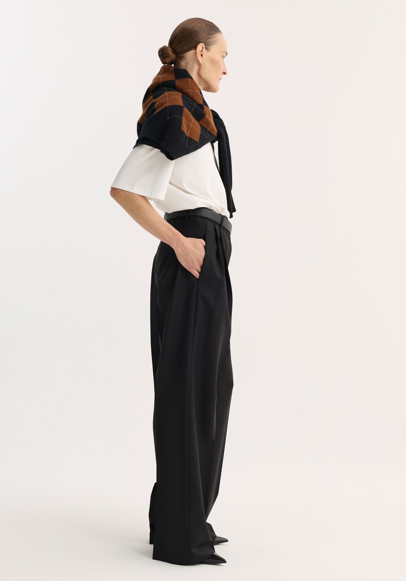 Mid-waist tailored trousers in black, featuring a wide-leg cut, double pleats, and a sleek, minimalist look with a draped checkered sweater.