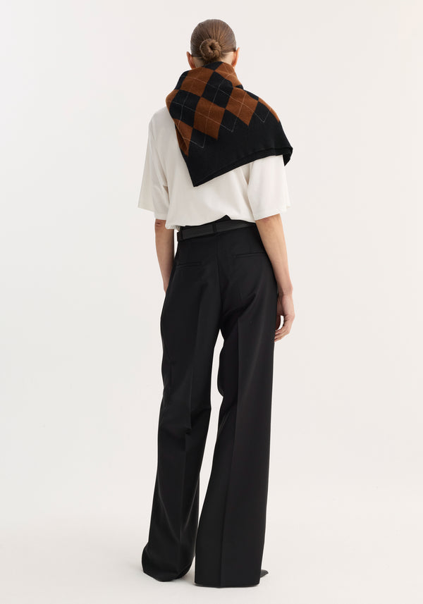 Back view of a person wearing mid-waist tailored trousers in black, featuring a wide-leg design and slim belt, styled with a draped argyle sweater.