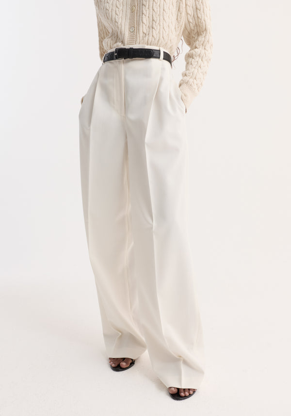 Mid-waist tailored trousers in off white, featuring a high-waisted, wide-leg design with double pleats, shown paired with a black belt and sandals.