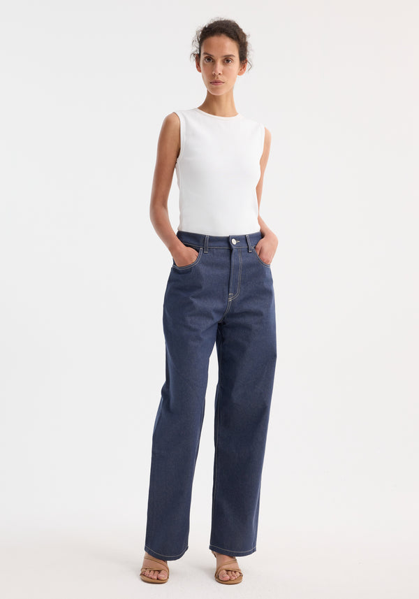 Woman wearing Signature baggy fit raw denim; fitted sleeveless top, high-waisted straight-leg jeans with a low-waist, wide-leg design, hands in pockets, and tan sandals.