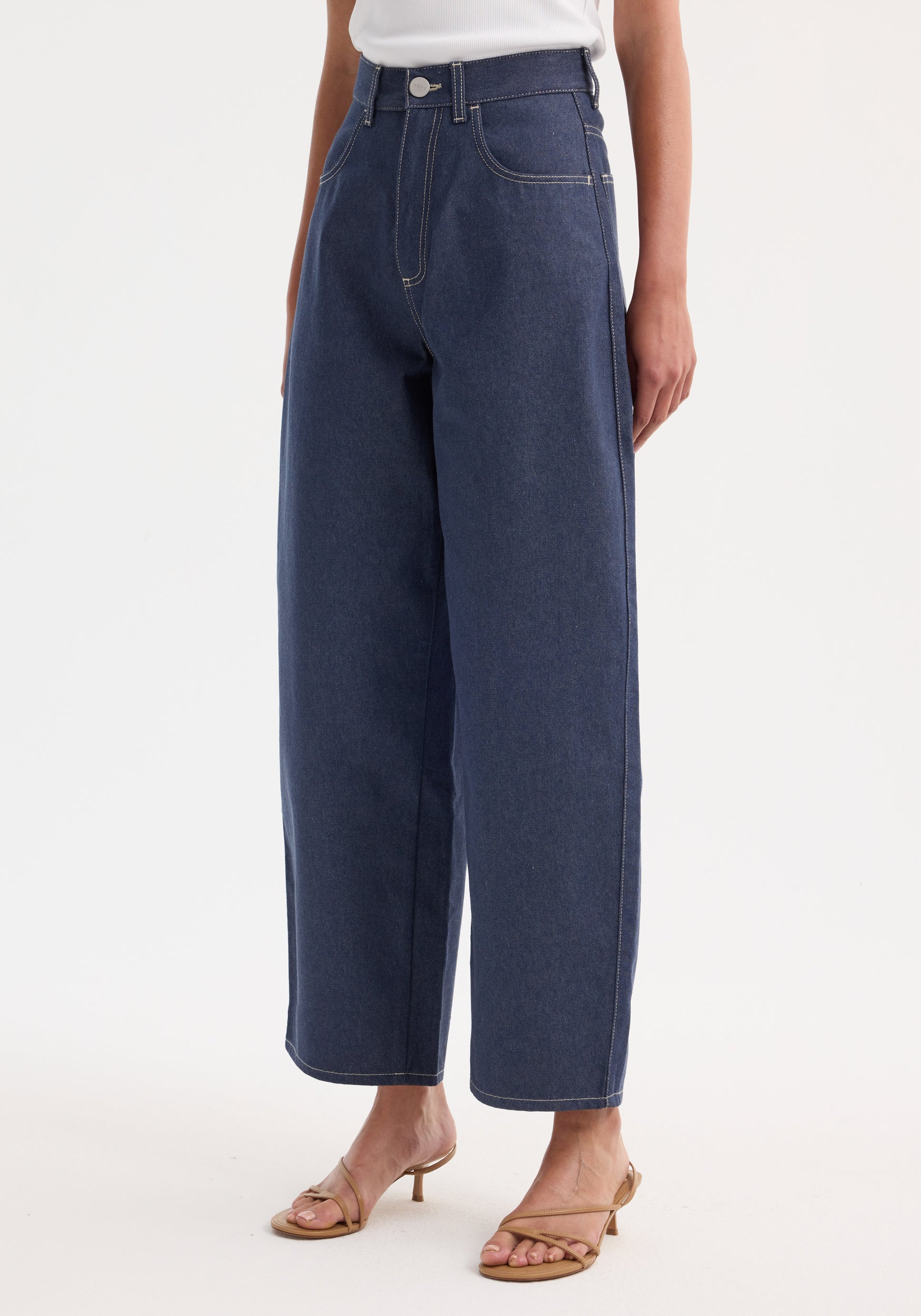 Barrel leg raw denim jeans with wide, curved legs made from pure Italian cotton, paired with tan heeled sandals, showcasing a timeless silhouette.