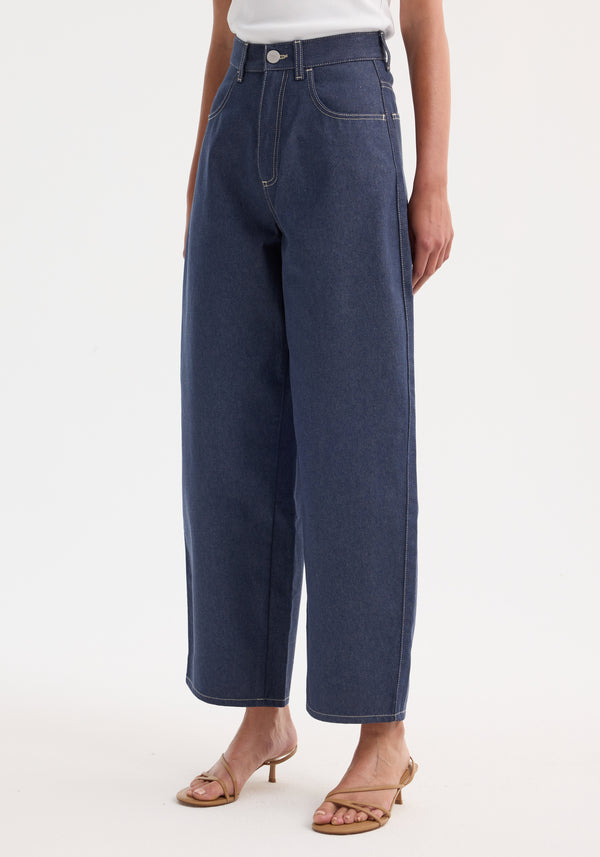 Barrel leg raw denim jeans with wide, curved legs made from pure Italian cotton, paired with tan heeled sandals, showcasing a timeless silhouette.