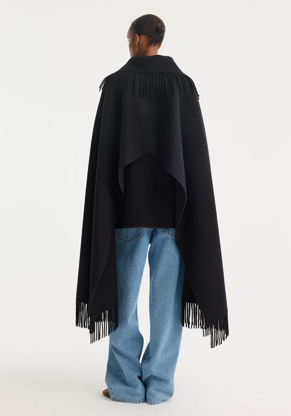 Fringe poncho double-faced wool | black, shown from behind, drapes over loose-fit jeans, featuring fringe detailing on shoulders and hem, offering warmth and elegance.