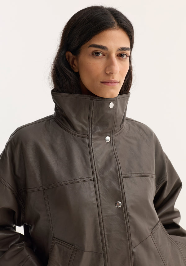 Reinvented leather jacket | earth: Model wears a structured, high-collared brown bomber jacket with snap buttons and topstitching, highlighting its relaxed, oversized fit in soft leather.