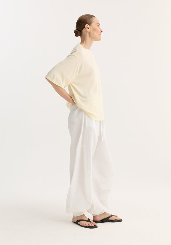 Profile view of a model wearing an oversized merino t-shirt with dropped shoulders and elbow-length sleeves, paired with voluminous drawstring pants and flip-flops.