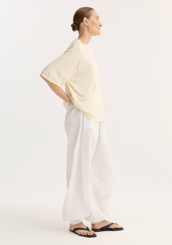 Person wearing an oversized merino t-shirt with drop shoulders and elbow-length sleeves, paired with wide-leg trousers and flip-flops, showcasing a relaxed silhouette.