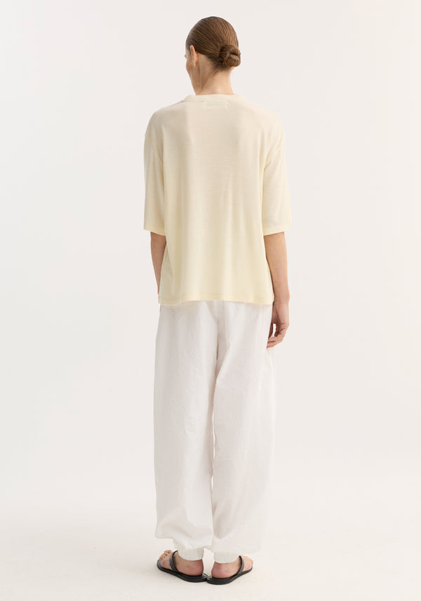 Model wearing oversized merino T-shirt with dropped shoulders and elbow-length sleeves, showcasing a relaxed fit, paired with billowy pants and black slide sandals.