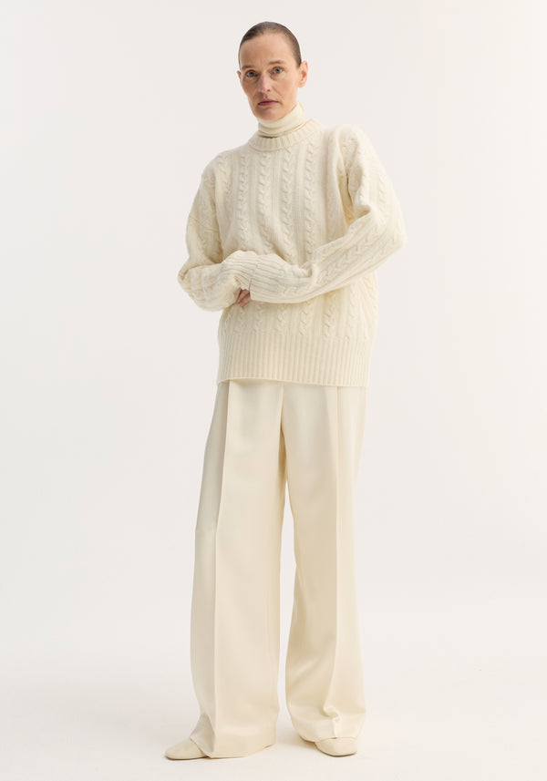 Model in Cable knit jumper | off white: oversized, pure wool with dropped shoulders and round neckline, styled over a turtleneck and wide-leg trousers.