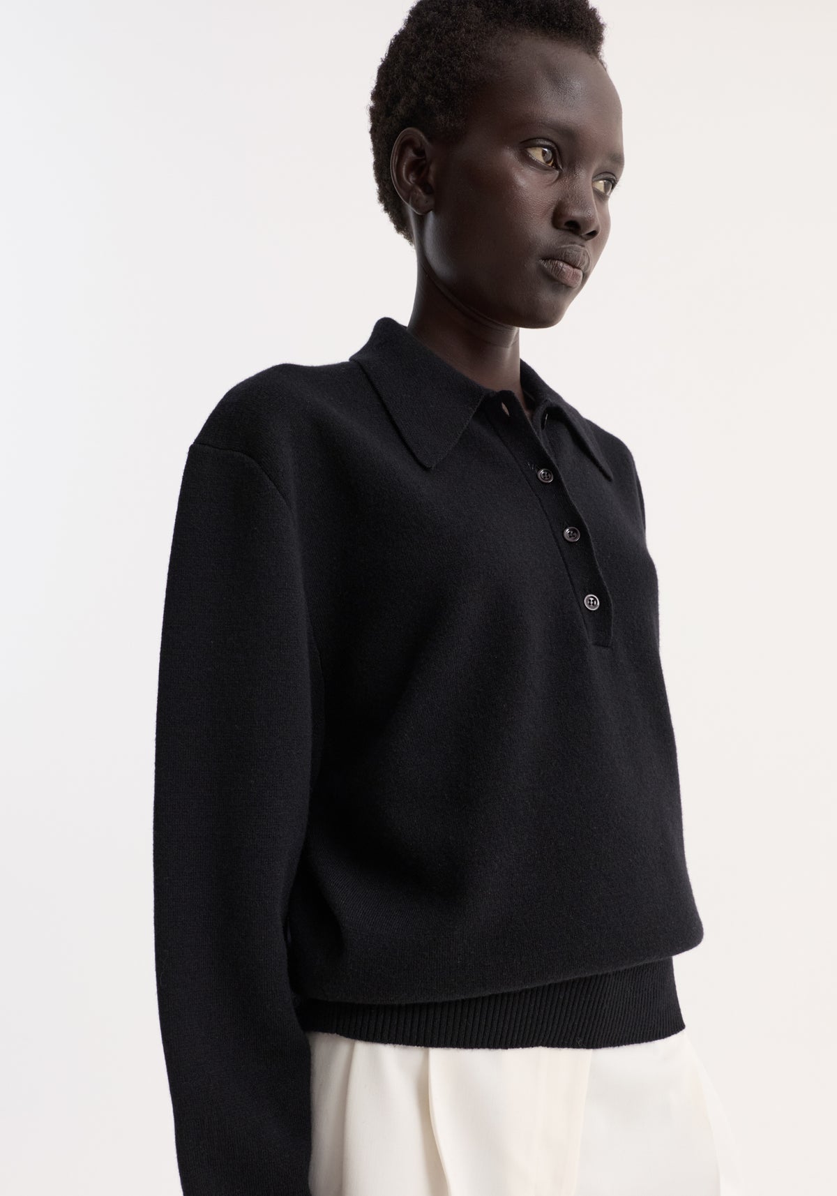 Compact knitted polo in wool-cashmere blend, featuring a structured collar, three-button placket, and rounded drop shoulders, worn by a model in white bottoms.