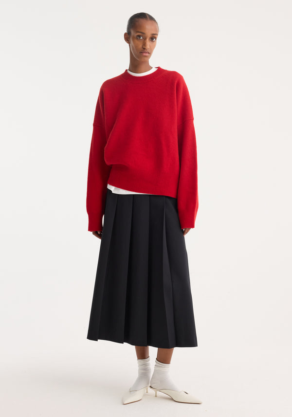 Person wearing a Boiled wool crewneck in a relaxed fit over a white top, paired with a black pleated skirt and white shoes.