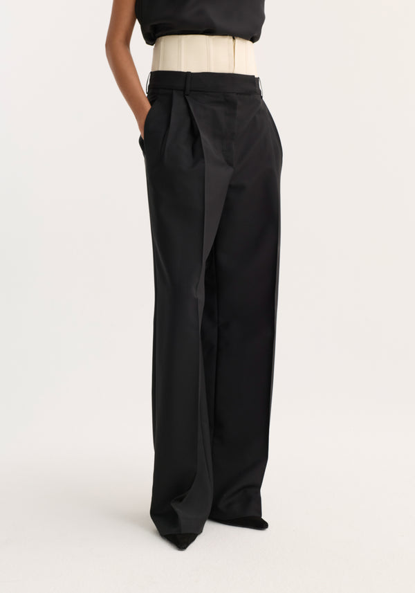 Model wearing Corset trousers | black, featuring high-waisted design, wide-leg cut, front pleats, and a draped flap detail. Corset belt enhances structure.
