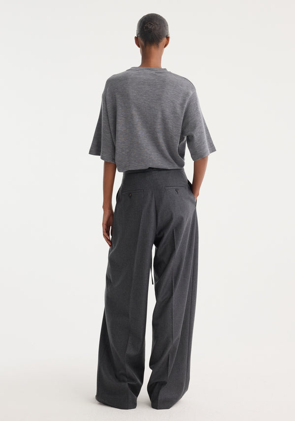 Back view of a person wearing relaxed soft wool trousers in dark grey melange with a wide leg and drawstring waistband, showcasing elegant tailoring and lightweight comfort.