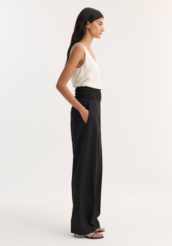 Cummerbund trousers in black, featuring a structured waistband with back shell buttons, side pockets, and a straight-leg fit, worn with strappy sandals.