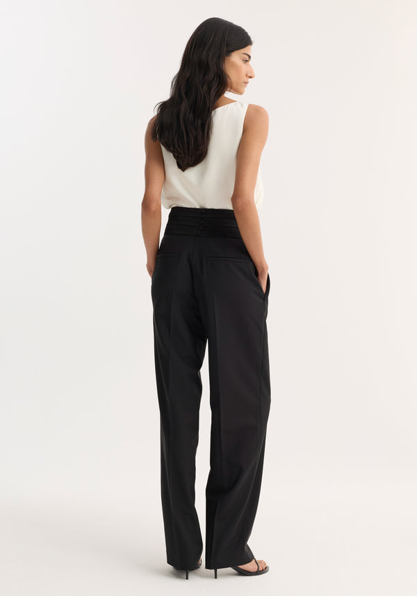 Woman wearing Cummerband trousers | black, featuring a structured satin waistband and wide-leg design, with hands in pockets, paired with heeled sandals.