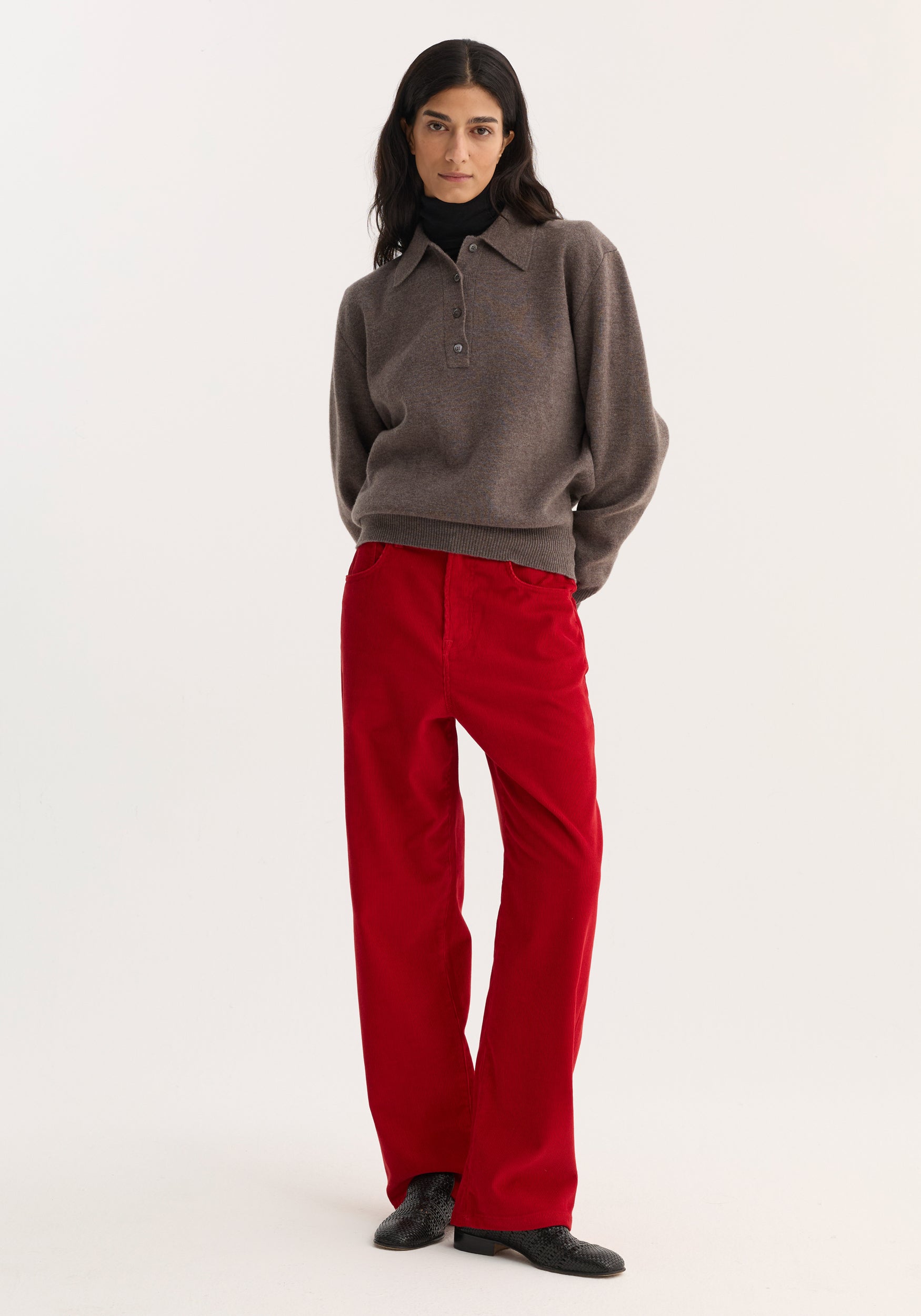 Model wearing Relaxed Corduroy Trousers in Rosso, styled with a charcoal-brown sweater and black turtleneck, showcasing a casual, utilitarian look.