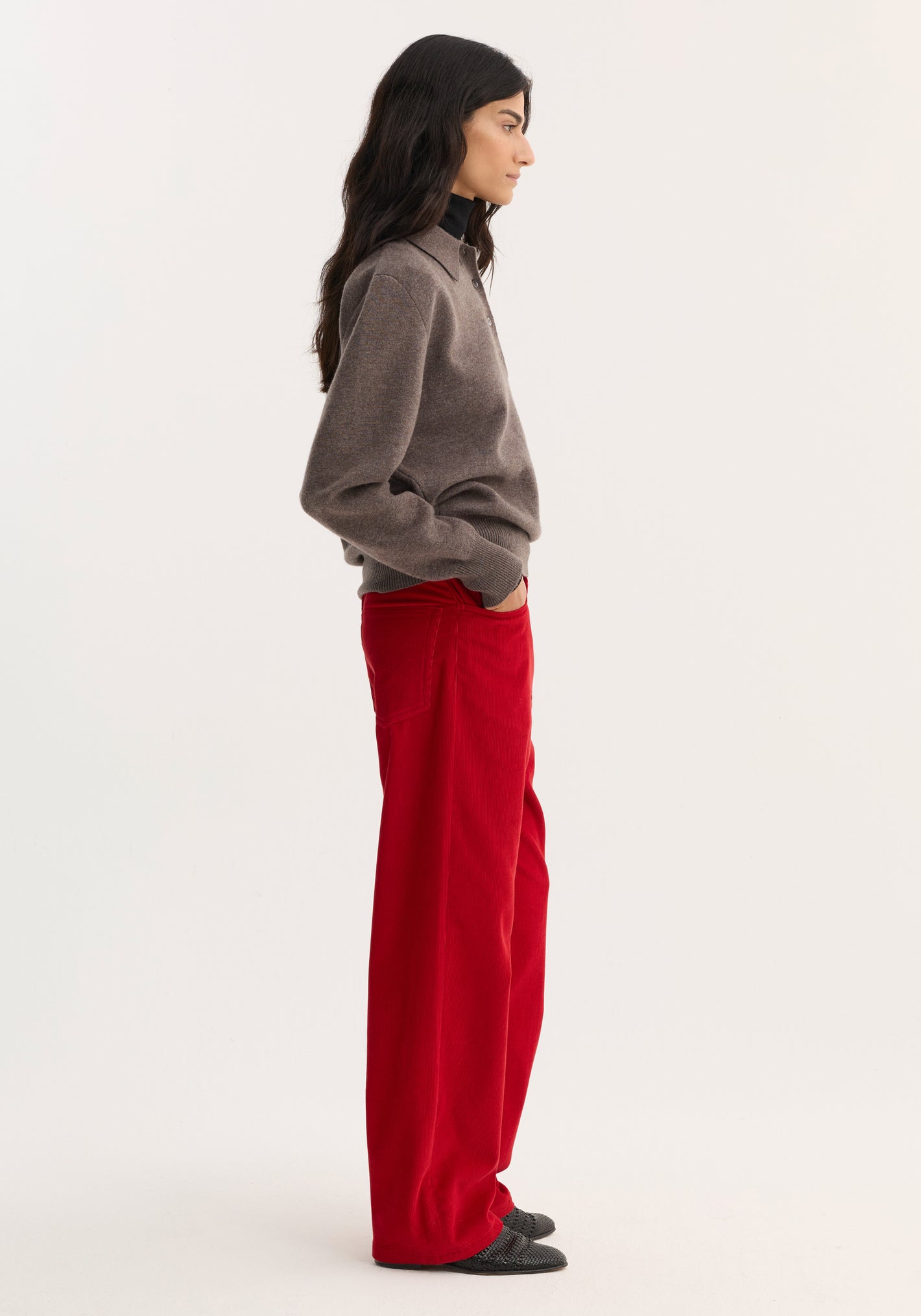 Woman in relaxed corduroy trousers | rosso, wearing a gray sweater and dark flat shoes. Trousers are wide-leg with front pockets, showcasing a casual yet stylish look.
