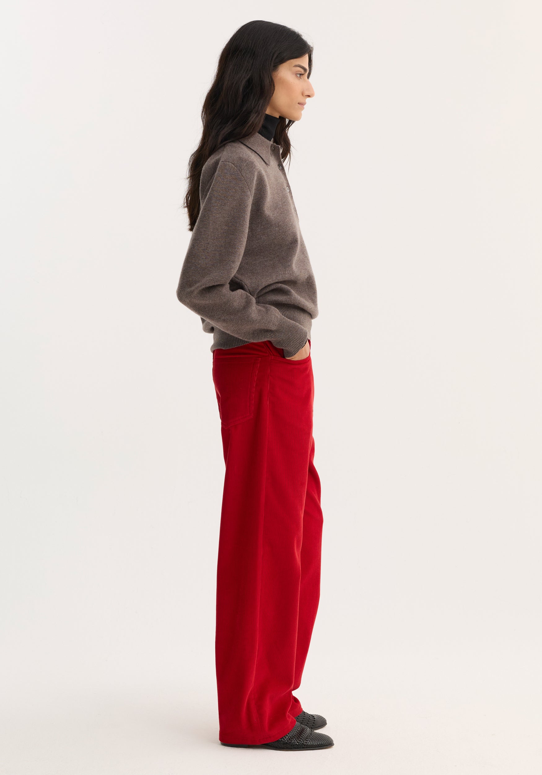 Woman in relaxed corduroy trousers | rosso, wearing a gray sweater and dark flat shoes. Trousers are wide-leg with front pockets, showcasing a casual yet stylish look.