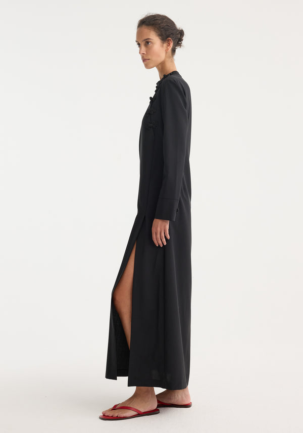 Model in profile wearing Pankou closure dress | black, with pankou closures, floor-length, side slit, long sleeves, styled with red flip-flops.