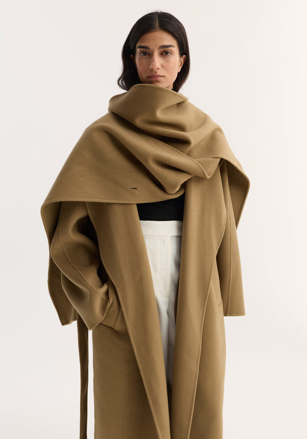 Woman wearing the Signature double-faced scarf coat in camel, featuring a double-layered scarf collar, double-breasted design, side pockets, and tailored long silhouette.