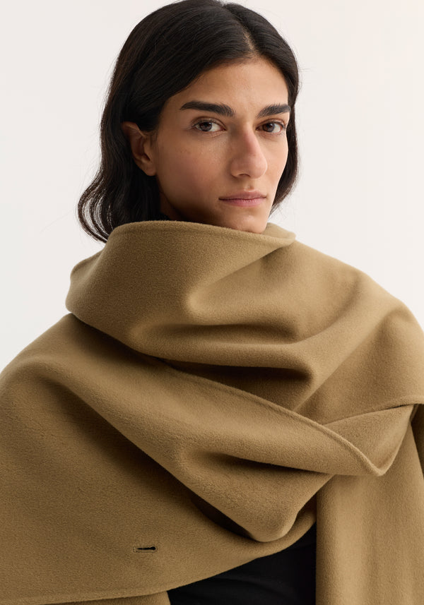 Close-up of a person wearing the Signature double-faced scarf coat in camel, showcasing its large wool wrap collar and tailored silhouette against a light background.