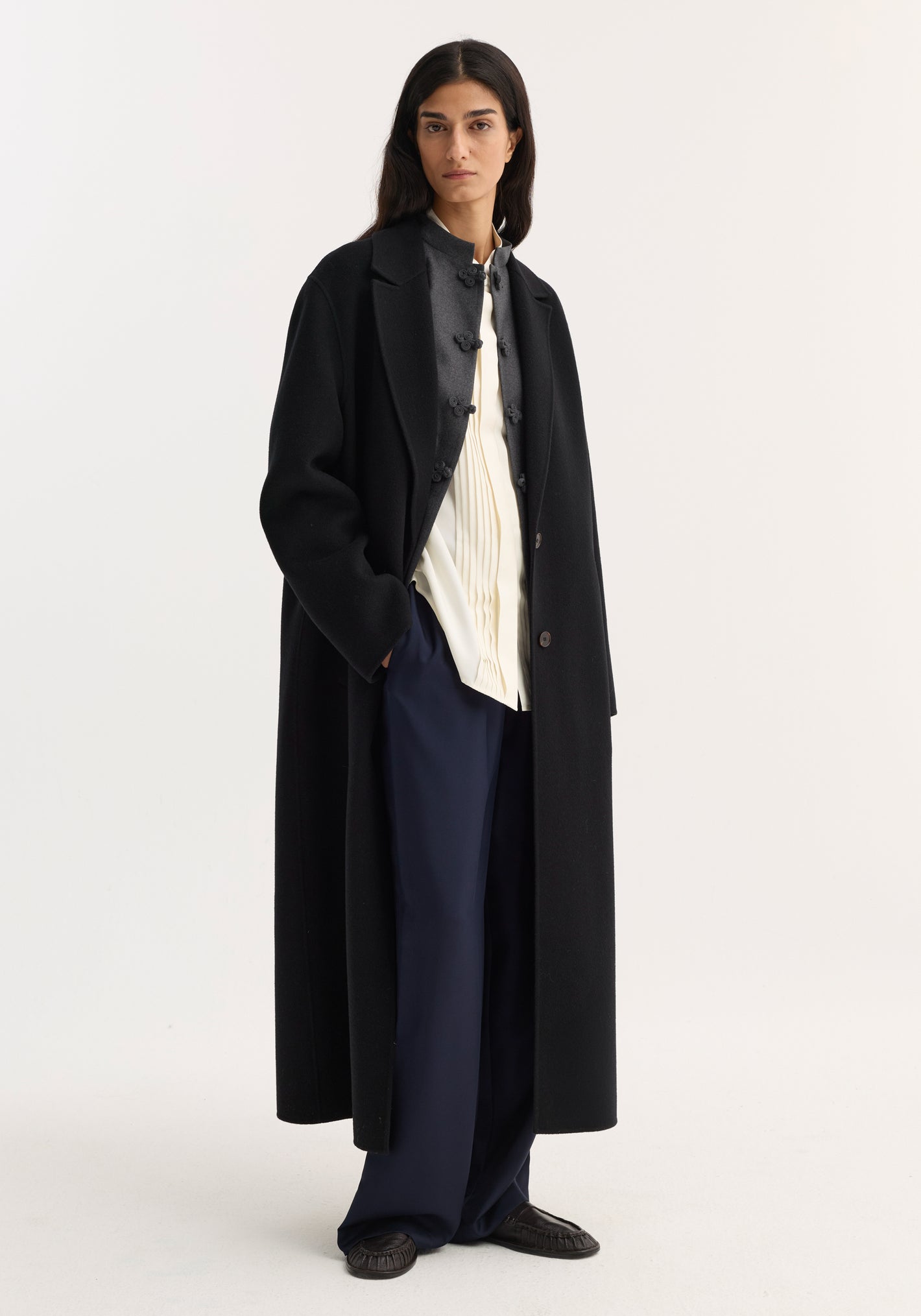 Model wearing a Double-faced coat | black, single-breasted, ankle-length, crafted from wool, with side pockets, over a charcoal jacket, cream blouse, and navy trousers.